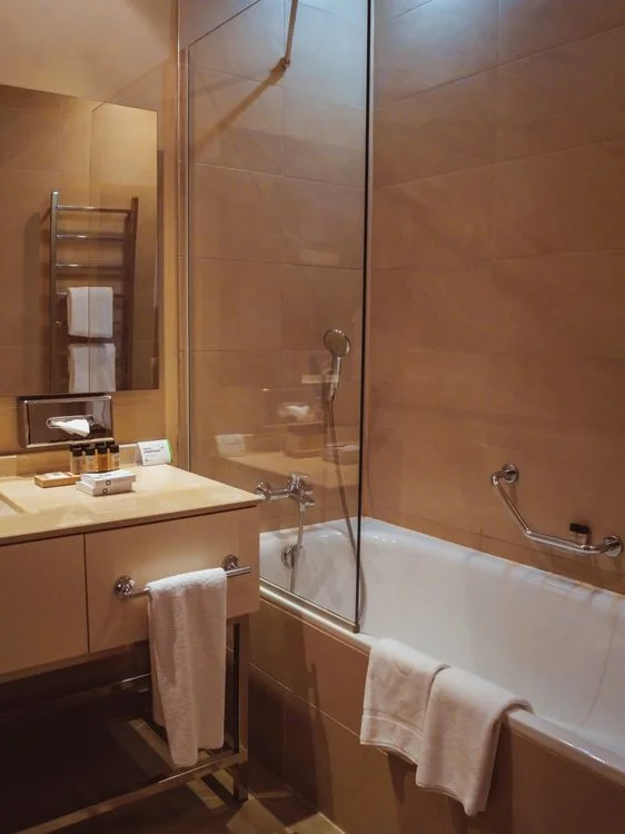 Hotel bathroom with a white built-in bathtub, glass shower screen and chrome grab bar