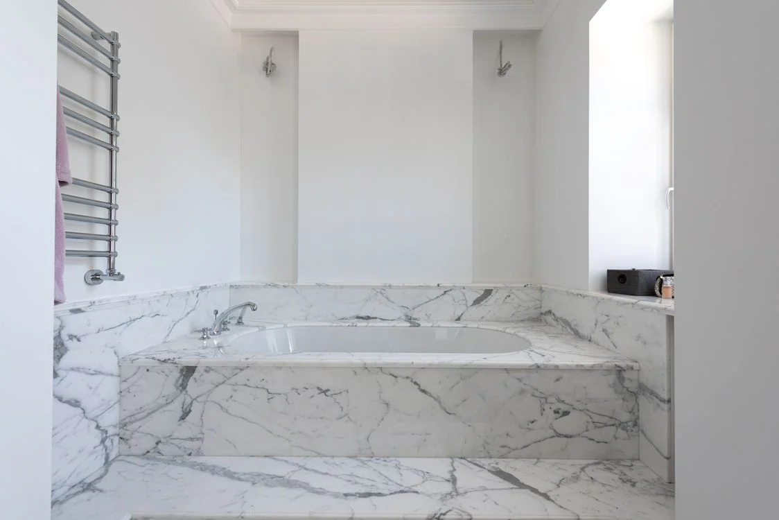 White built-in bathtub with a marble surround and chrome fixtures